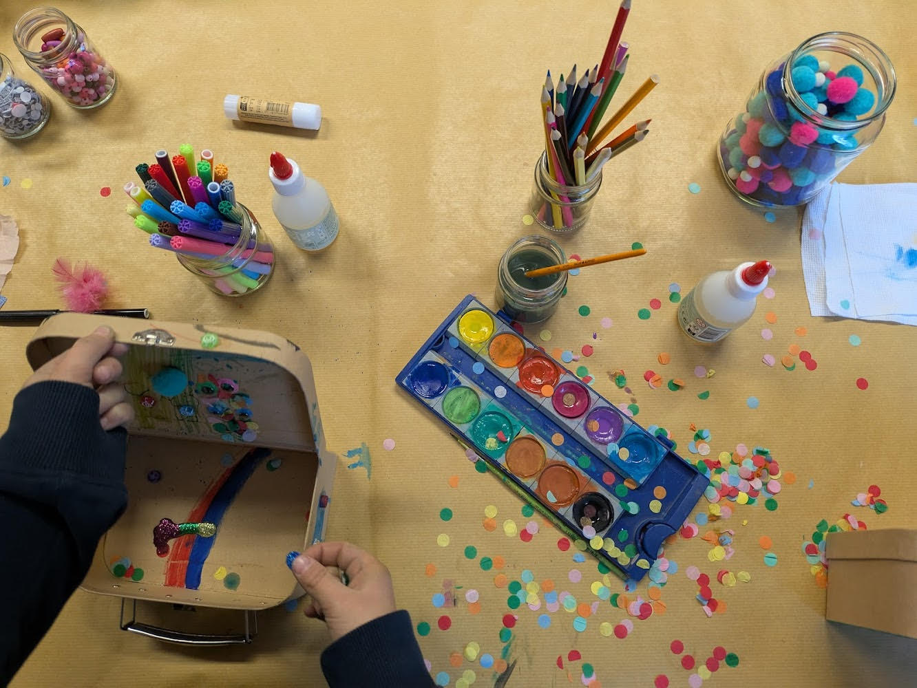 Nahaufnahme: ein Koffer wird mit Wasserfarben und Konfetti gestaltet